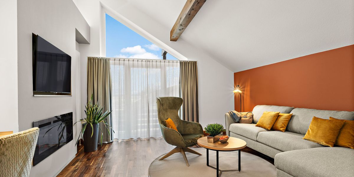 Wohnbereich der Komfort-Suite im Hotel Churfürstenhof mit Sofa, Sessel, Kamin und großem Giebelfenster
