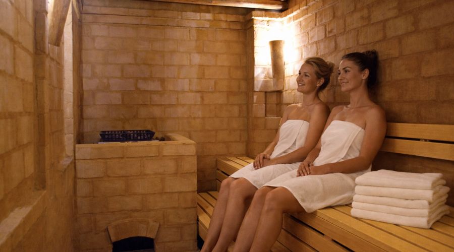 Zwei Frauen in Handtüchern entspannen auf der Holzbank der Lehmsauna im Hotel Churfürstenhof