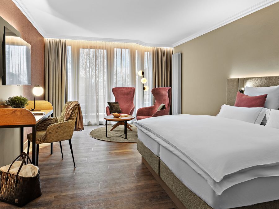 Zimmer Komtess im Wellnesshotel Churfürstenhof: Doppelbett, rote Sessel und Schreibtisch in warmen Farben