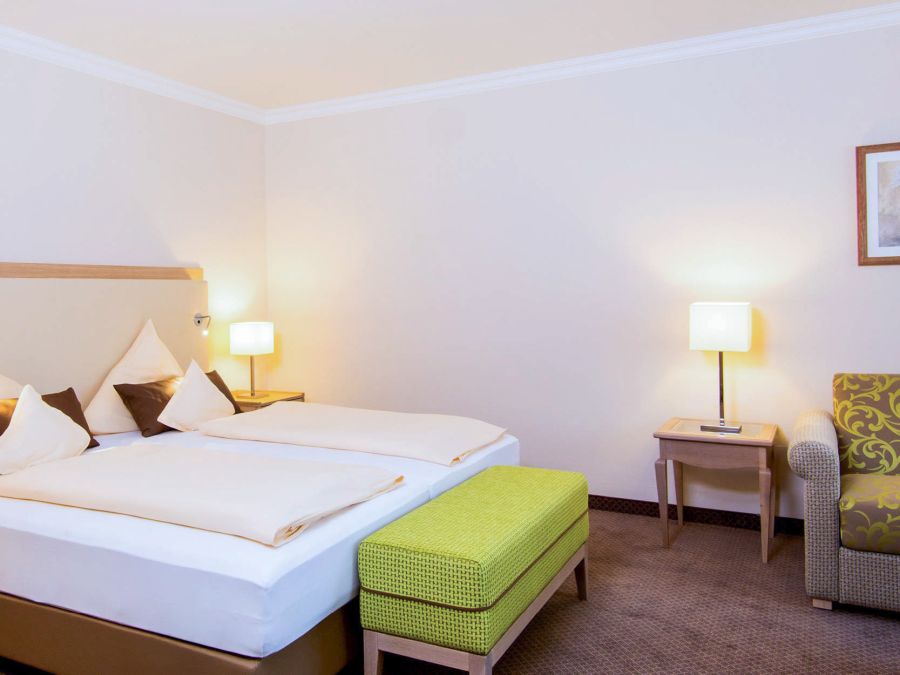 Doppelbett mit weißer Bettwäsche und grüner Sitzbank im Zimmer Baroness, Hotel Churfürstenhof Bad Birnbach