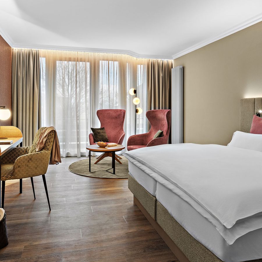 Zimmer Komtess im Wellnesshotel Churfürstenhof: Doppelbett, rote Sessel und Schreibtisch in warmen Farben
