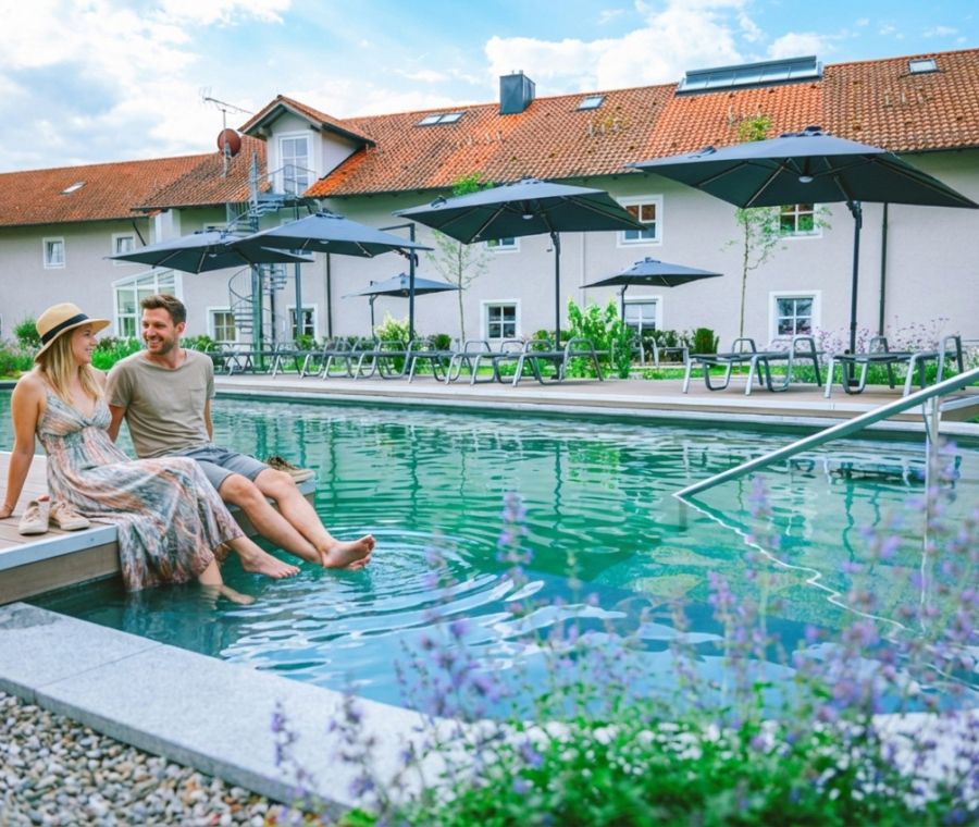 Paar sitzt am Rand des Außenpools des Hotels Churfürstenhof, dahinter Sonnenschirme und Liegen