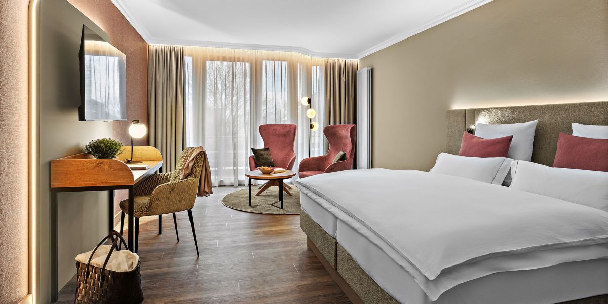 Zimmer Komtess im Wellnesshotel Churfürstenhof: Doppelbett, rote Sessel und Schreibtisch in warmen Farben