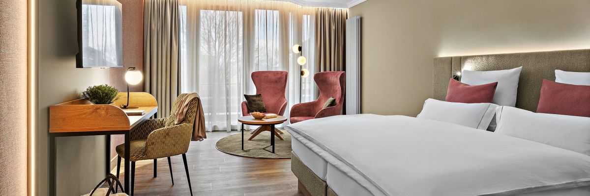 Zimmer Komtess im Wellnesshotel Churfürstenhof: Doppelbett, rote Sessel und Schreibtisch in warmen Farben