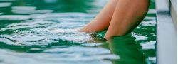 Beine tauchen vom Beckenrand ins grünliche Wasser des Naturpools im Hotel Churfürstenhof
