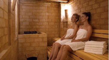 Zwei Frauen in Handtüchern entspannen auf der Holzbank der Lehmsauna im Hotel Churfürstenhof