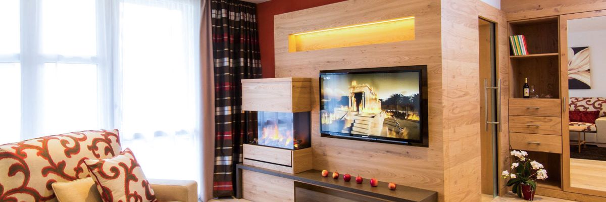 Wohnzimmer der Suite Royal im Churfürstenhof Bad Birnbach mit Sofa, Kamin und TV-Wand aus Holz