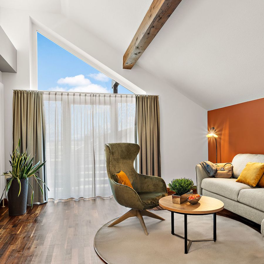 Wohnbereich der Komfort-Suite im Hotel Churfürstenhof mit Sofa, Sessel, Kamin und großem Giebelfenster