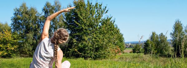 Frau bei Yoga im Grünen auf einer Holzplattform
