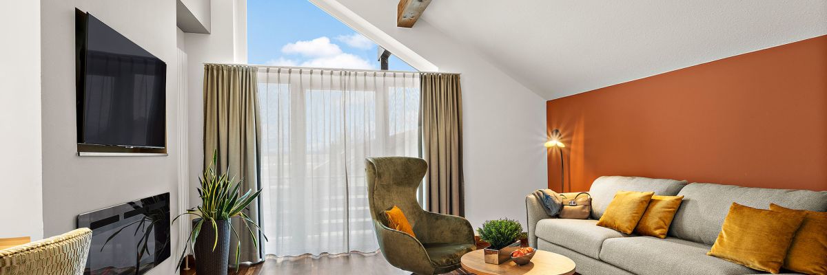 Wohnbereich der Komfort-Suite im Hotel Churfürstenhof mit Sofa, Sessel, Kamin und großem Giebelfenster