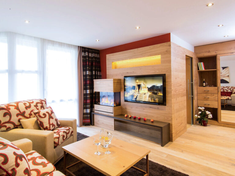 Wohnzimmer der Suite Royal im Churfürstenhof Bad Birnbach mit Sofa, Kamin und TV-Wand aus Holz