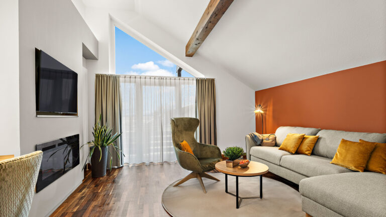 Wohnbereich der Komfort-Suite im Hotel Churfürstenhof mit Sofa, Sessel, Kamin und großem Giebelfenster