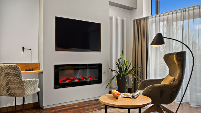 Wohnbereich der Komfort-Suite im Wellnesshotel Churfürstenhof mit Elektrokamin, TV, Sessel und Stehlampe
