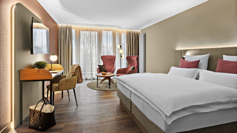 Zimmer Komtess im Wellnesshotel Churfürstenhof: Doppelbett, rote Sessel und Schreibtisch in warmen Farben