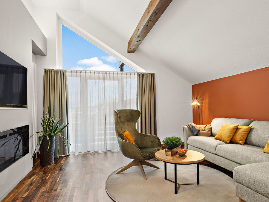 Wohnbereich der Komfort-Suite im Hotel Churfürstenhof mit Sofa, Sessel, Kamin und großem Giebelfenster